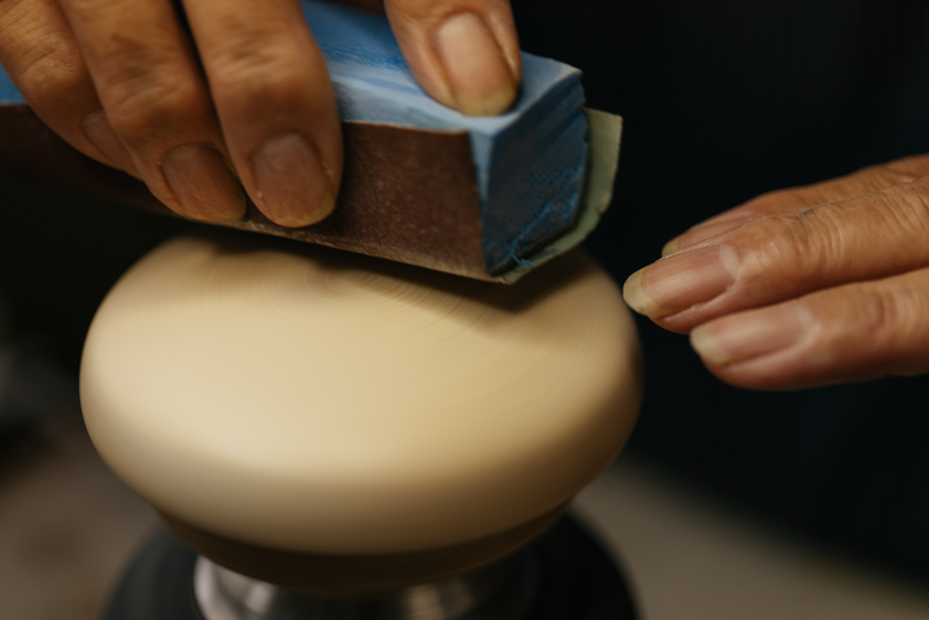 An artisan sands the curved wooden headphone housing in an Audio-Technica workshop