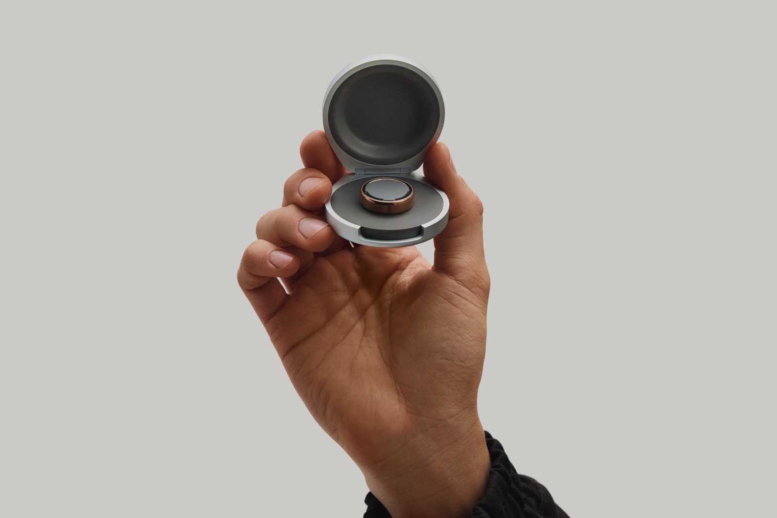 A hand holding an open Oura Ring 5 charging case with a ring inside